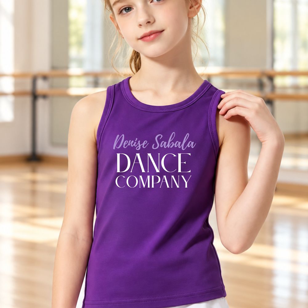 A young girl wearing a purple sleeveless tank top with 'Denise Sabala DANCE COMPANY' printed in white text, standing in a dance studio with wooden floors and barres in the background.