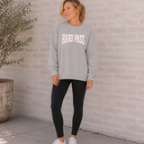 Woman wearing a gray sweatshirt with 'HARD PASS' text against a stone wall.