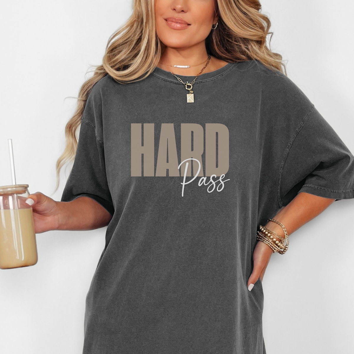 Person wearing a gray t-shirt with 'HARD Pass' text, holding a drink.