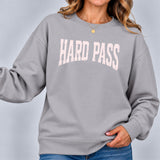 Woman wearing the stone gray Hard Pass sweatshirt with light pink lettering, paired with blue jeans, in a close-up studio shot.