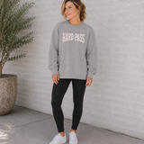 Woman wearing a gray sweatshirt with 'HARD PASS' text, standing against a light gray wall.