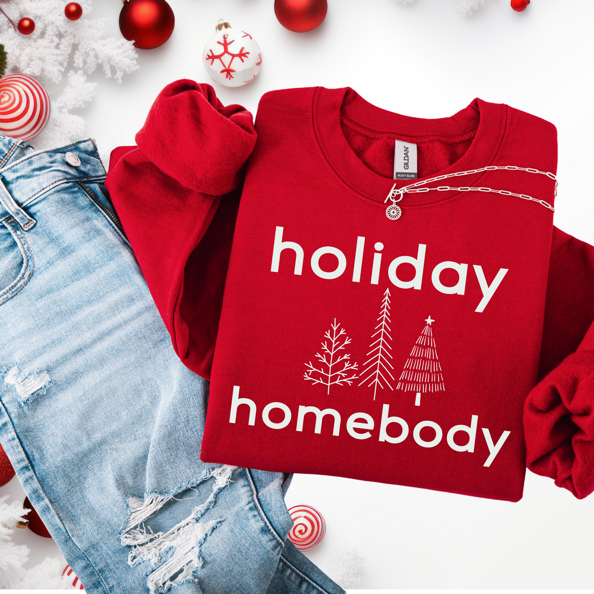 Red sweatshirt with 'holiday homebody' text and Christmas-themed decorations on a white background