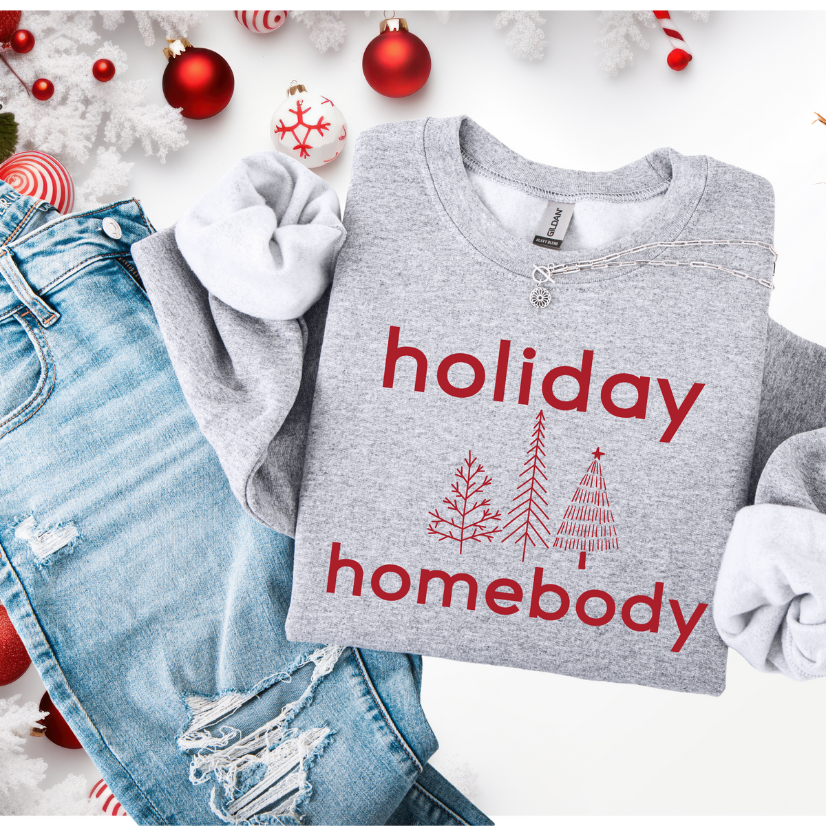 Gray sweatshirt with 'holiday homebody' text and Christmas tree designs on a festive background.