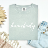Light green Comfort Colors t-shirt with 'homebody' text on a white background with denim jeans and decorative elements.
