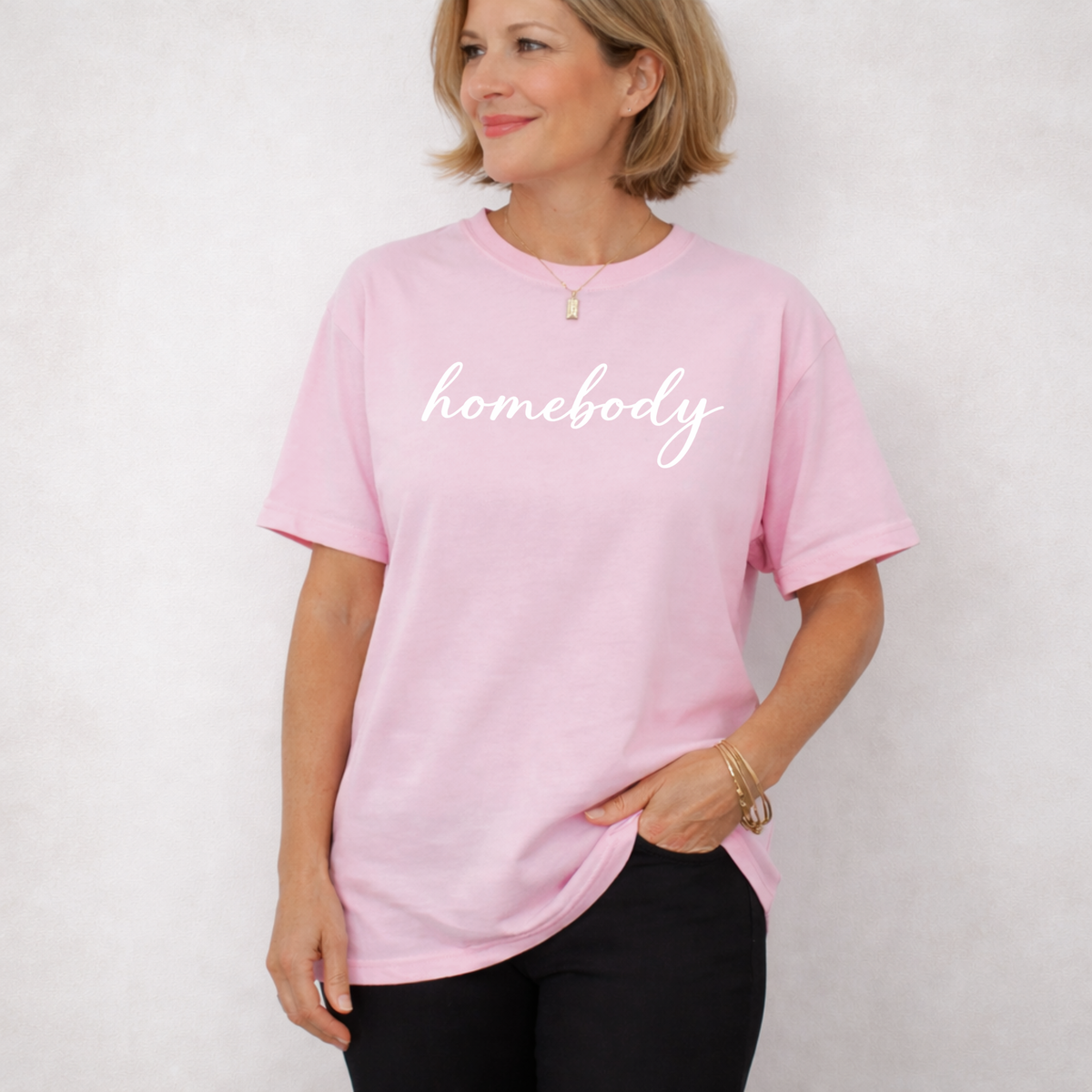 A woman standing with a light pink shirt on that says "homebody"
