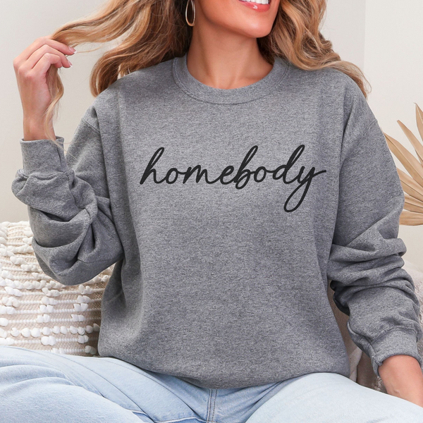 Person wearing a gray sweatshirt with 'homebody' text, sitting indoors.