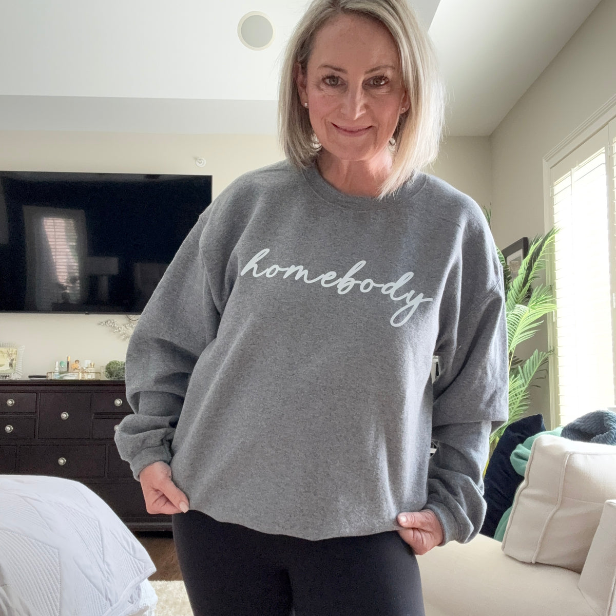 Person wearing a gray sweatshirt with 'nobody' printed on it, standing in a room.