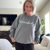 Person wearing a gray sweatshirt with 'nobody' printed on it, standing in a room.