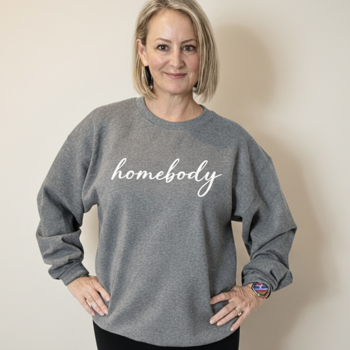 Woman wearing a gray sweatshirt with 'homebody' text on a beige background
