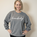 Woman wearing a gray sweatshirt with 'homebody' text on a beige background
