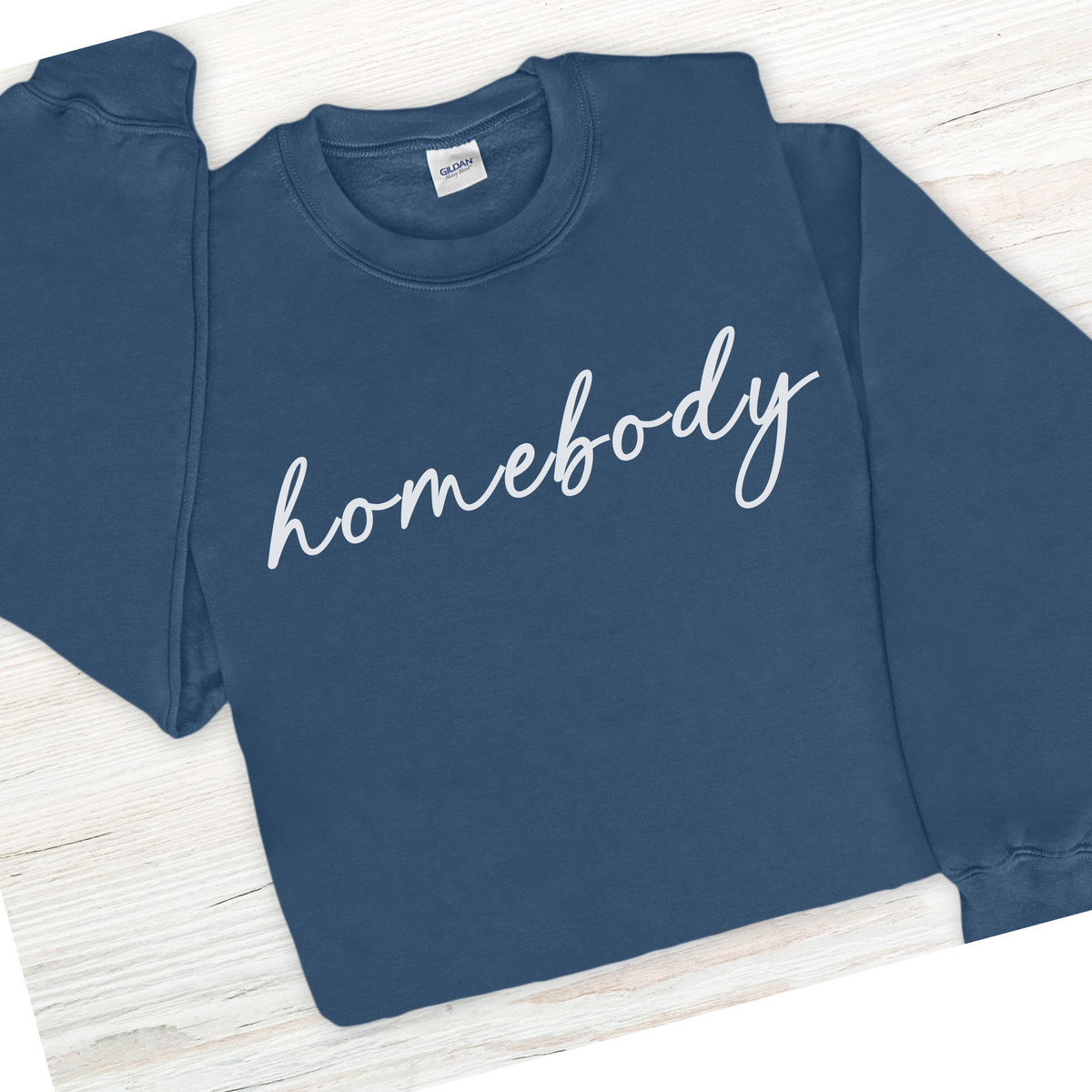 Blue sweatshirt with 'homebody' text on a wooden surface