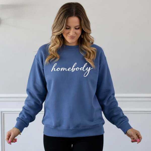 Woman wearing a blue sweatshirt with 'homebody' text against a plain background