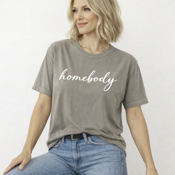 Woman wearing a light brown t-shirt with 'homebody' text on a white background