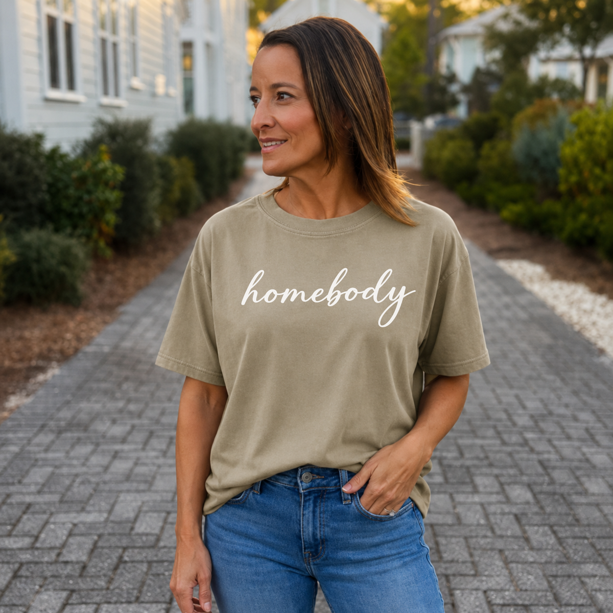 A woman standing outside with a khaki shirt on that says "homebody" in script writing
