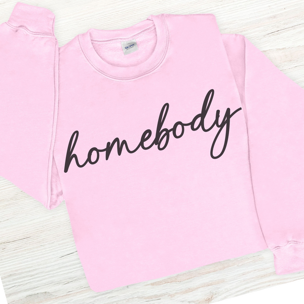 Pink sweatshirt with 'homebody' text on a light wooden surface