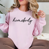 Person wearing a pink sweatshirt with 'homebody' text, holding a mug.