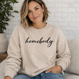 Woman wearing a beige sweatshirt with 'homebody' text, sitting on a couch.