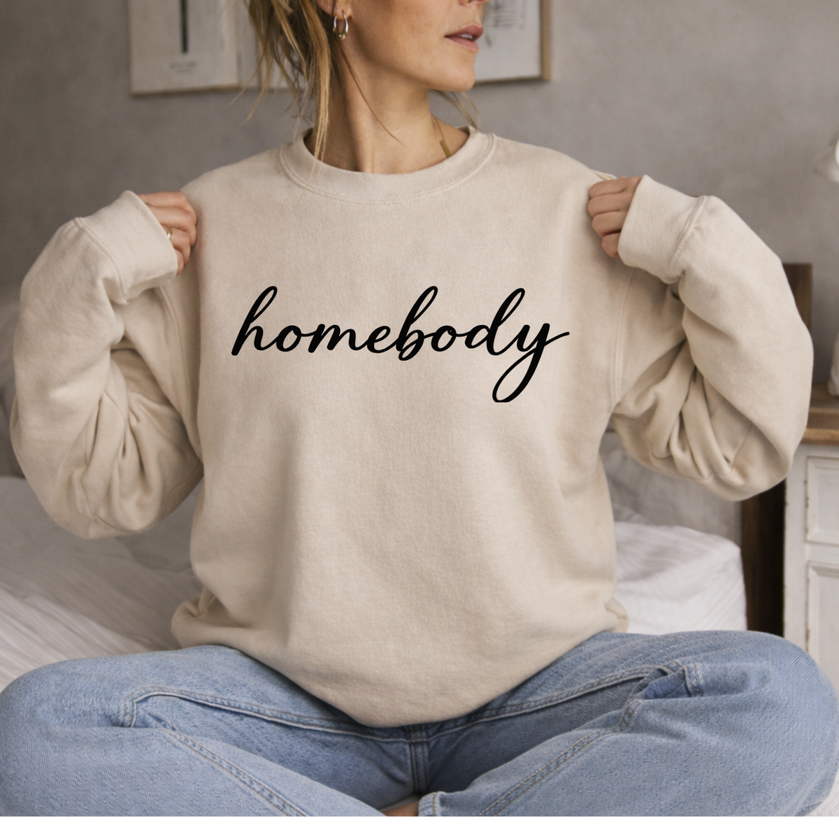 Person wearing a beige sweatshirt with 'homebody' text, sitting indoors.