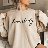 Person wearing a beige sweatshirt with 'homebody' text in a casual setting.
