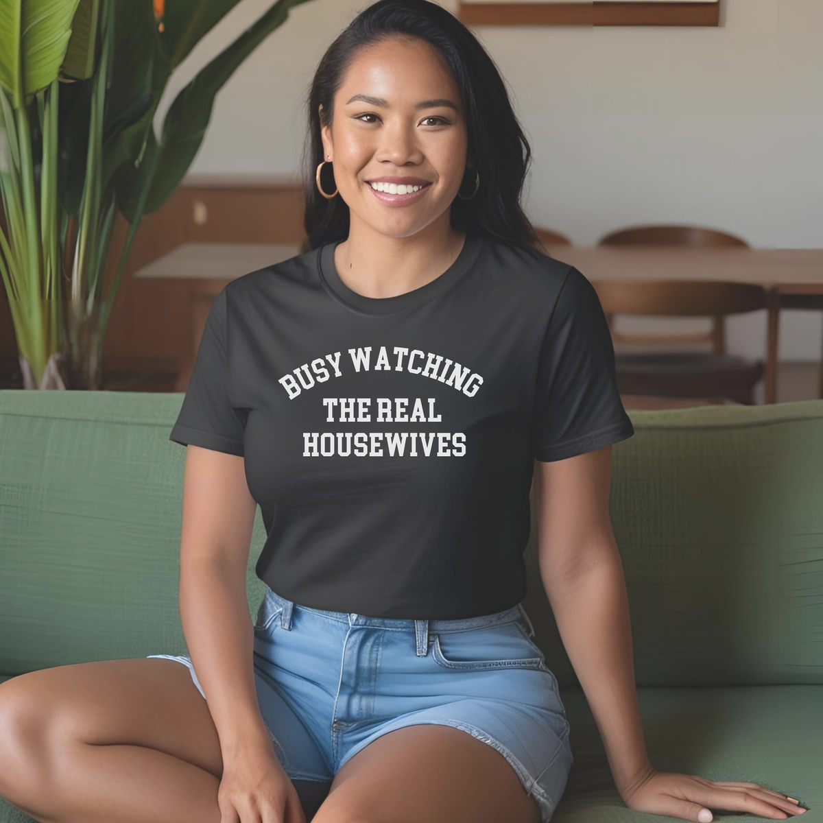 Woman wearing a black t-shirt with text, sitting on a green couch.