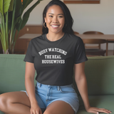 Woman wearing a black t-shirt with text, sitting on a green couch.