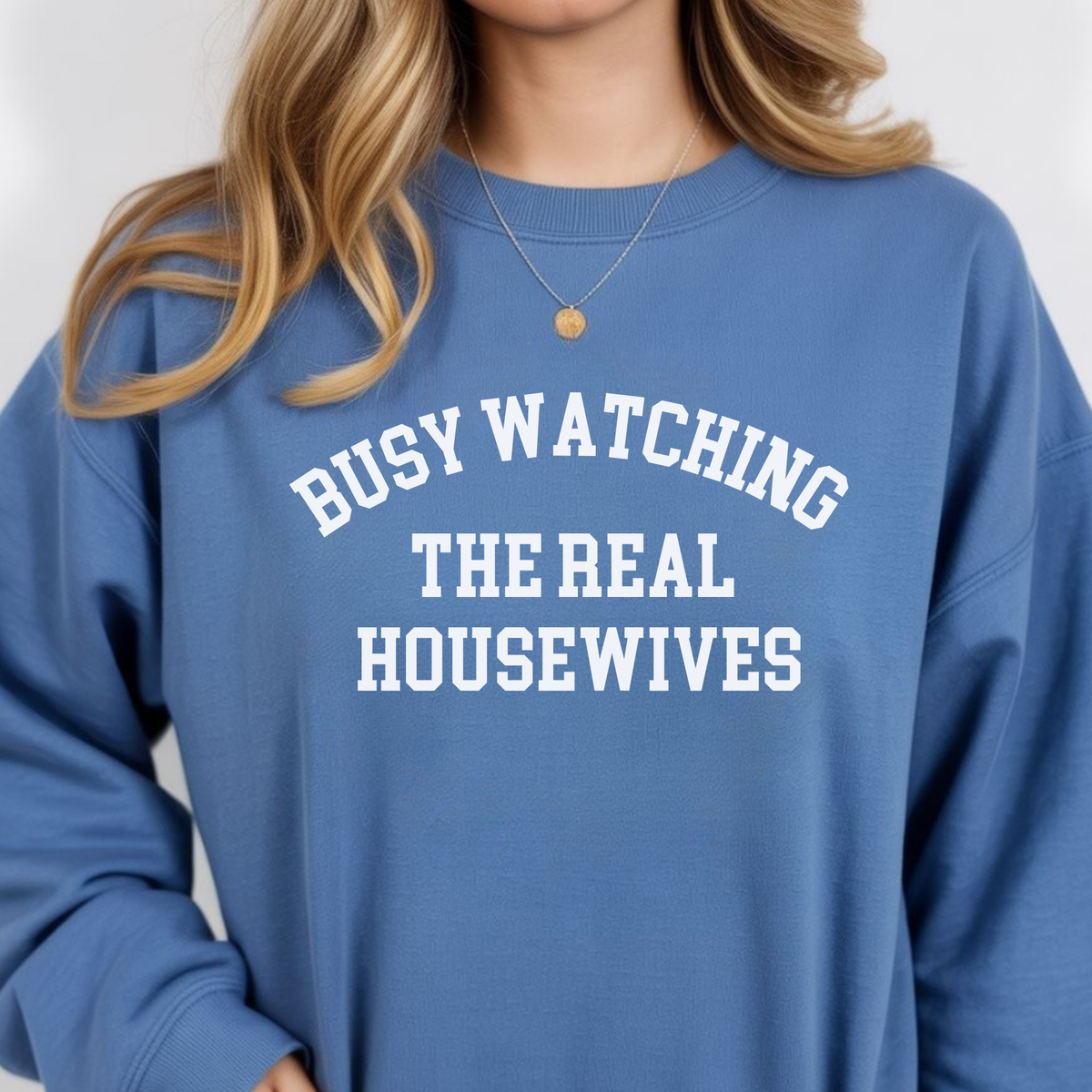 A woman wearing a blue sweatshirt with text 'BUSY WATCHING THE REAL HOUSEWIVES' on a plain background