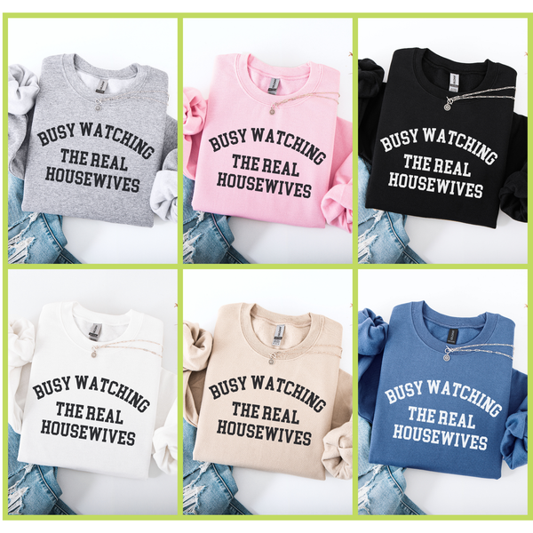 Collage of six crewneck sweatshirts in different colors (Gray, Pink, Black, White, Sand, Blue) with 'BUSY WATCHING THE REAL HOUSEWIVES' text.