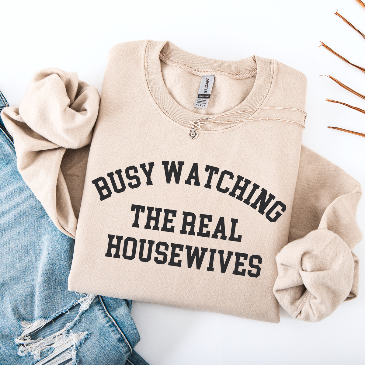 Sand Beige folded sweatshirt with 'BUSY WATCHING THE REAL HOUSEWIVES' text on a white background
