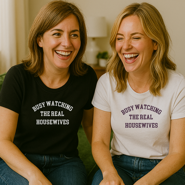 Two women sitting on a sofa wearing shirts that say "Busy Watching the Real Housewives."