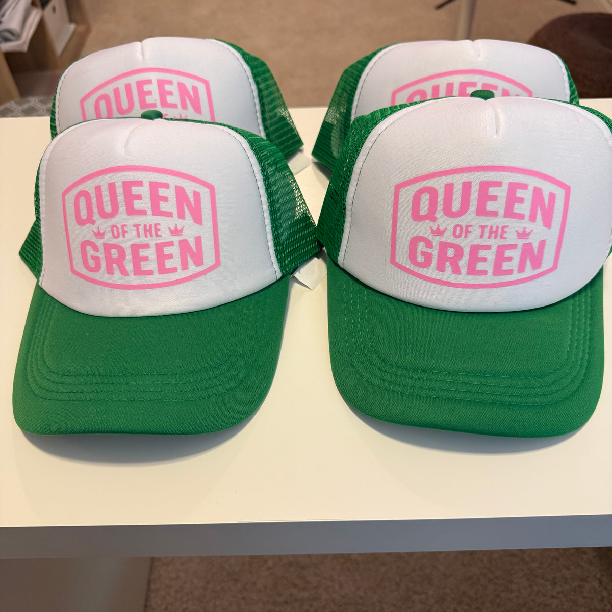 Green and white caps with 'Queen of the Green' text on a stand.