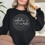 Person wearing a black sweatshirt with 'inhale exhale' over a faded circle design.