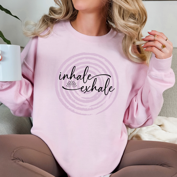 Person wearing a pink sweatshirt with 'inhale exhale' design over a faded circle design, holding a mug.