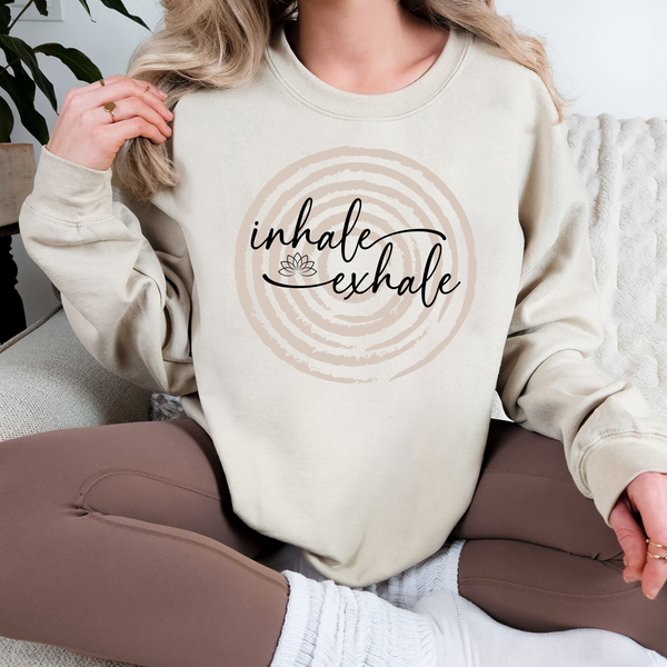 Person wearing a beige sweatshirt with 'inhale exhale' over a circle design.