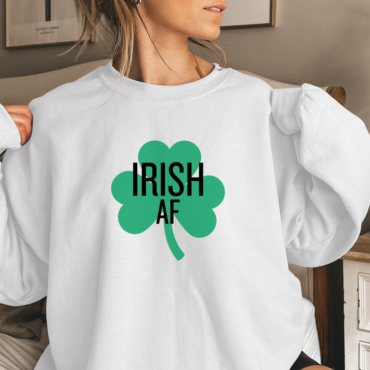 A woman wearing a white sweatshirt with a green shamrock and 'IRISH AF' text.