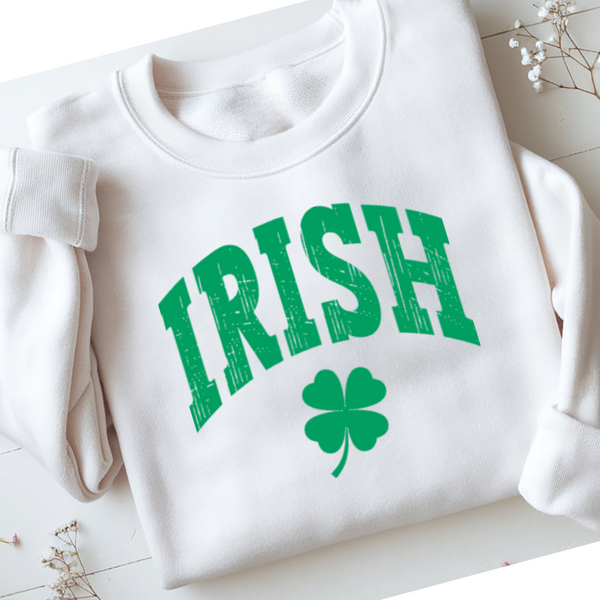 White sweatshirt with green 'IRISH' text and clover leaf on a light wooden surface.