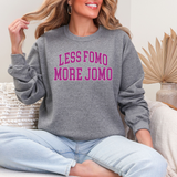 Person wearing a gray sweatshirt with 'LESS FOMO MORE JOMO' text, sitting on a couch.