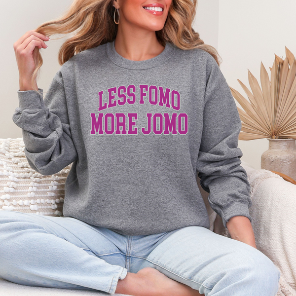 Person wearing a gray sweatshirt with 'LESS FOMO MORE JOMO' text, sitting on a couch.