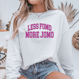 Person wearing a white sweatshirt with pink text 'LESS FOMO MORE JOMO' in a casual setting.