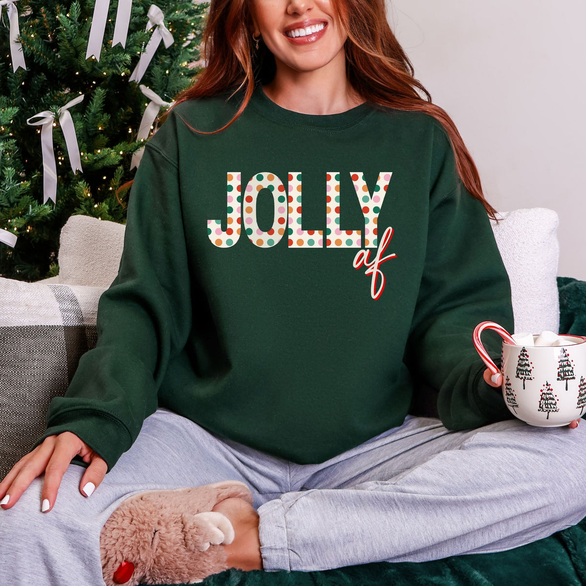 Person wearing a green sweatshirt with 'Jolly AF' text, sitting in front of a Christmas tree.