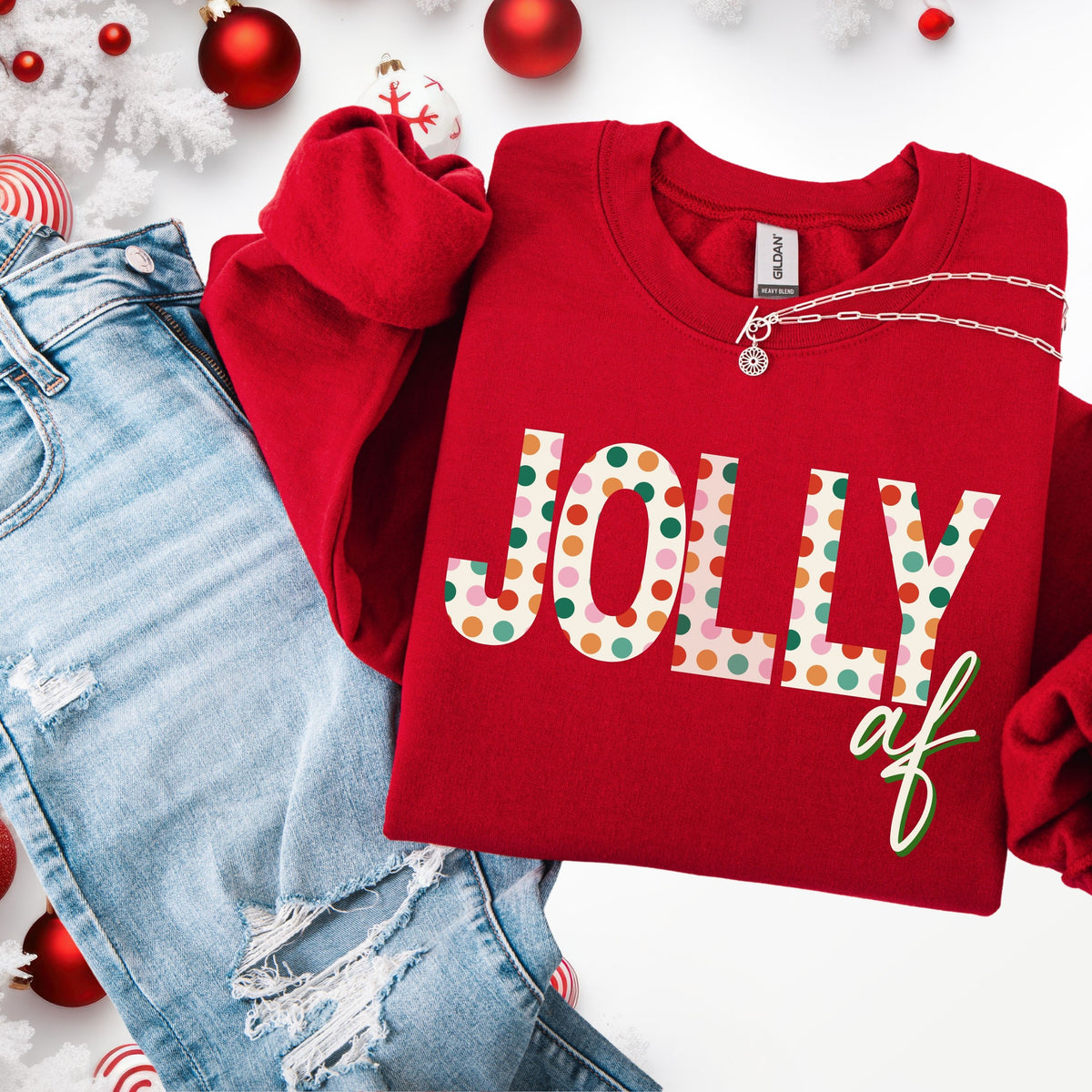 Red sweatshirt with 'Jolly af' text, paired with ripped jeans and Christmas decorations on a white background.