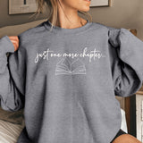 Person wearing a gray sweatshirt with 'just one more chapter...' text and book graphic.