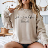 Woman wearing a beige sweatshirt with 'just one more chapter...' text and book graphic.