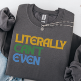 A folded dark gray crewneck sweatshirt with the phrase 'LITERALLY CAN'T EVEN' printed in yellow, green, and blue block letters. A silver chain necklace is draped across the collar area.