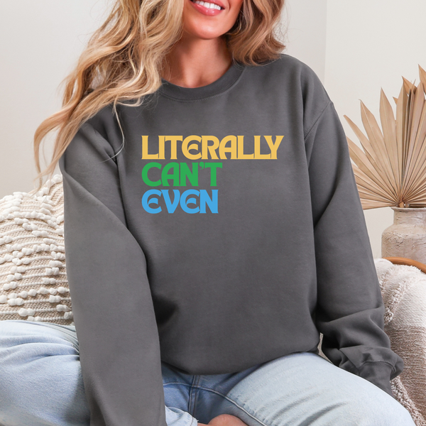 Person wearing a gray sweatshirt with colorful text that says LITERALLY CAN'T EVEN sitting on a couch.