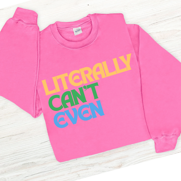 Pink sweatshirt with colorful text that says LITERALLY CAN'T EVEN on a white wooden surface