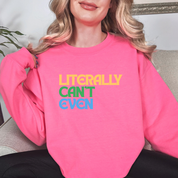 Person wearing a pink sweatshirt with colorful text that says LITERALLY CAN'T EVEN sitting on a couch.