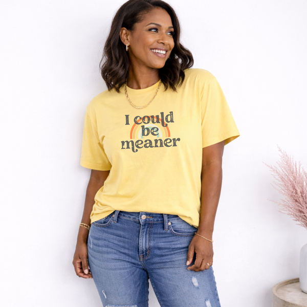 Woman wearing a yellow t-shirt with "I could be meaner" text, standing against a white background