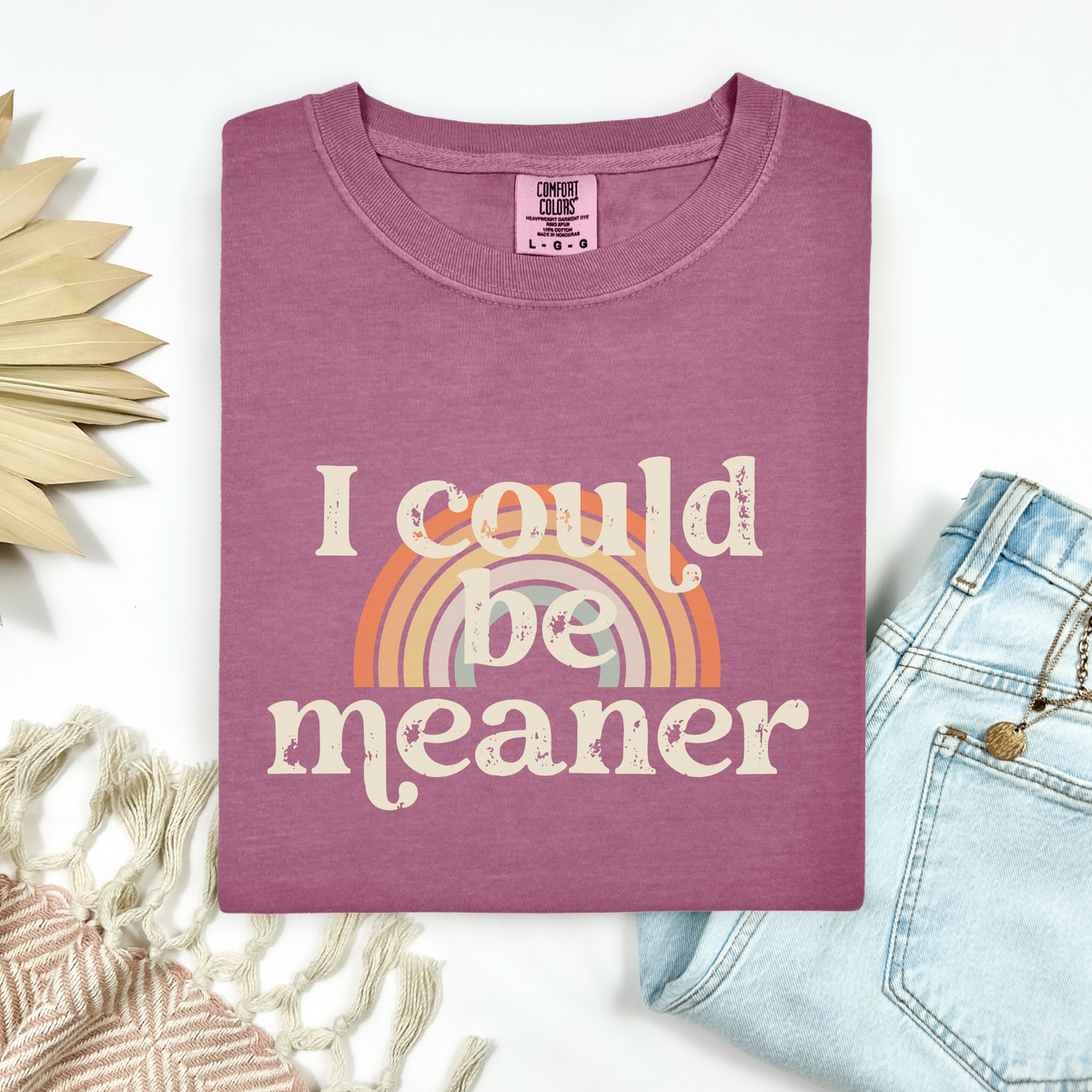 Berry Pink t-shirt with 'I could be meaner' text and rainbow graphic, placed on a white surface with decorative elements.