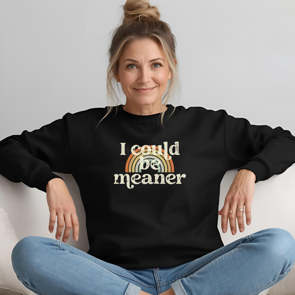 Woman wearing a black sweatshirt with 'I could be meaner' text and rainbow design.