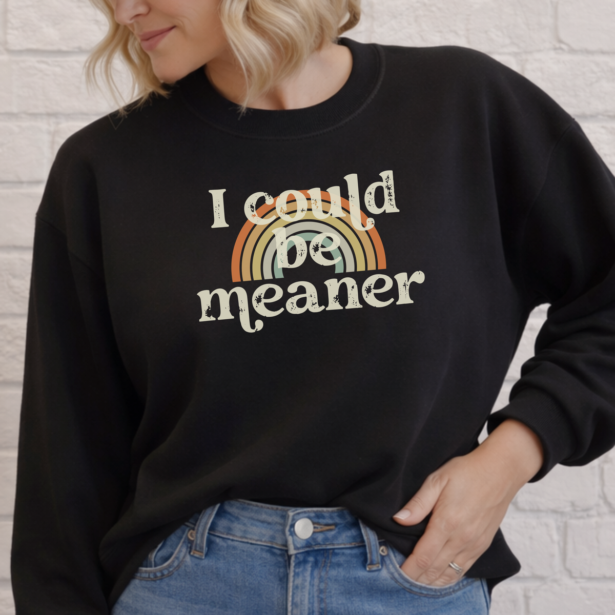 Person wearing a black sweatshirt with a colorful rainbow design and text against a light gray brick wall.